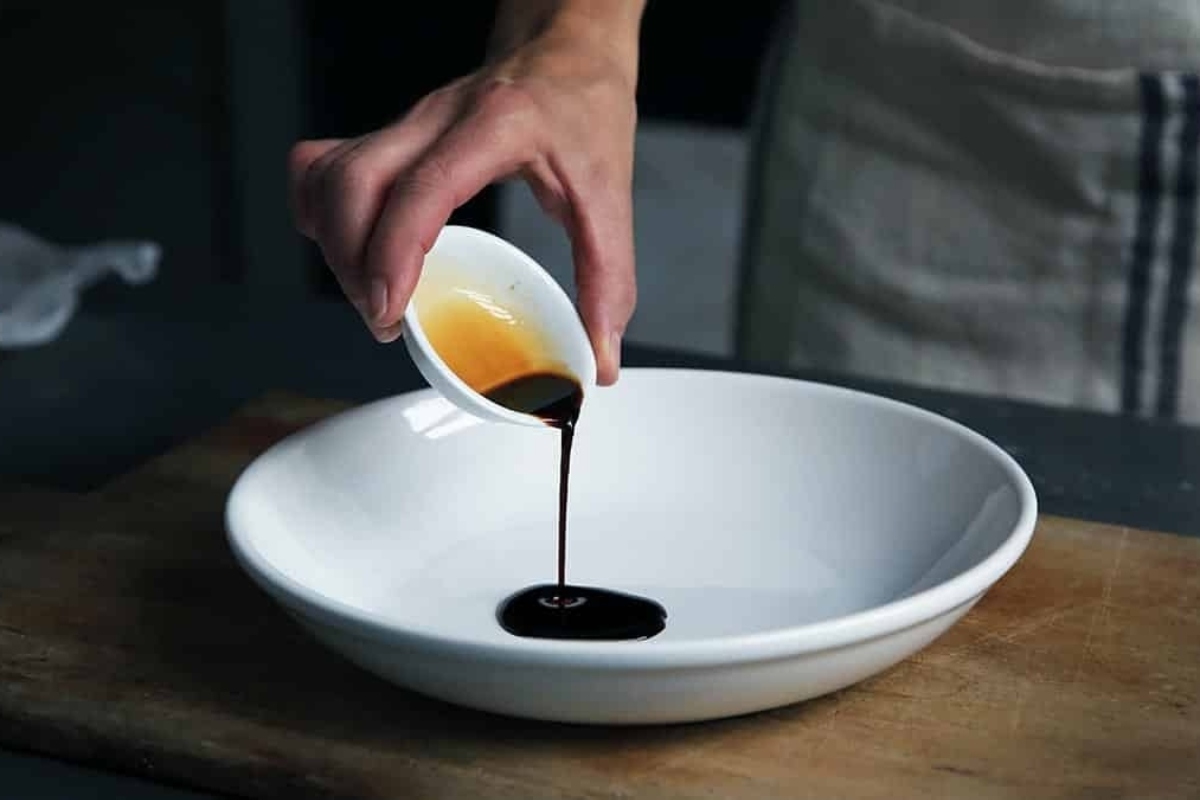 A person pouring a sauce into a white bowl.