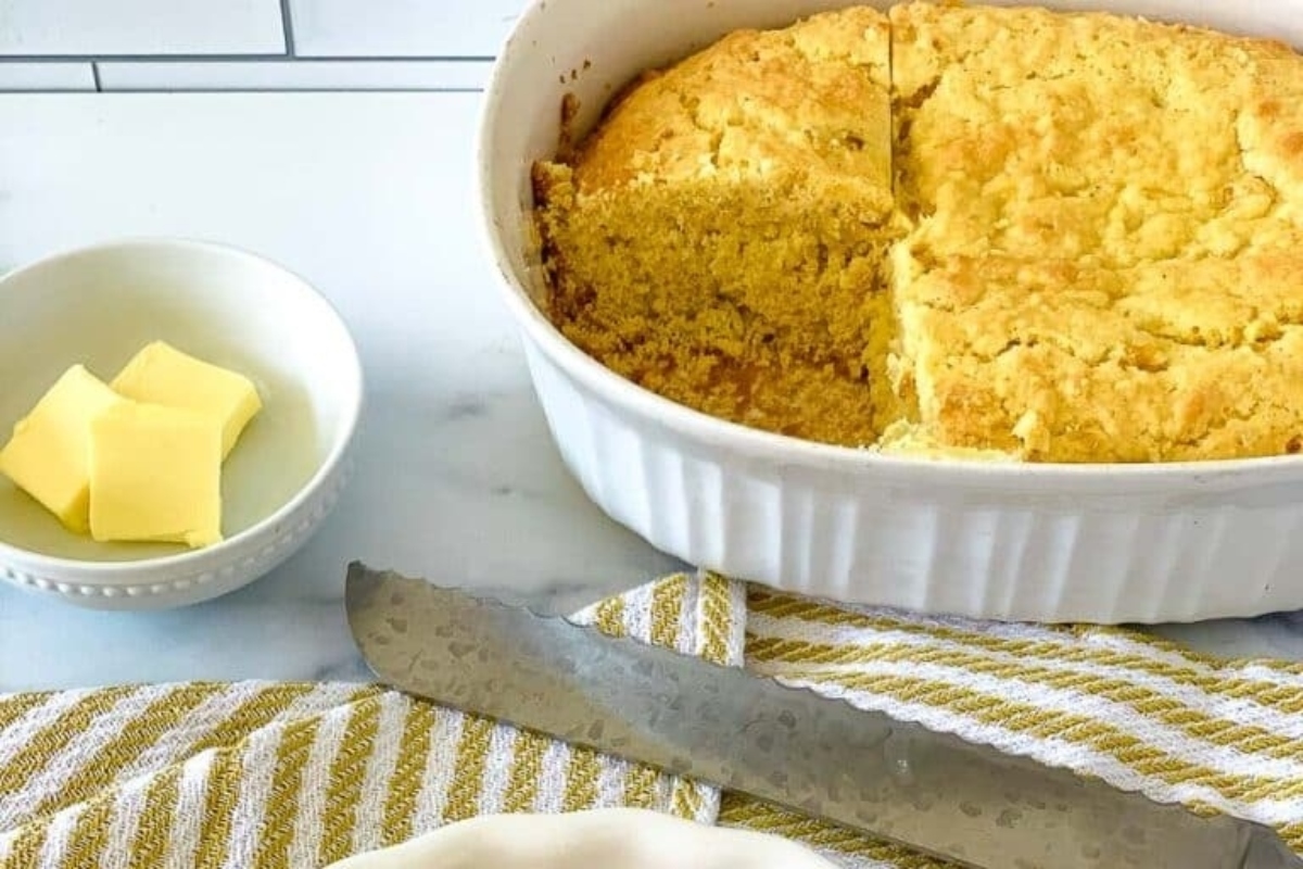 Cornbread in a white dish with a knife and butter.