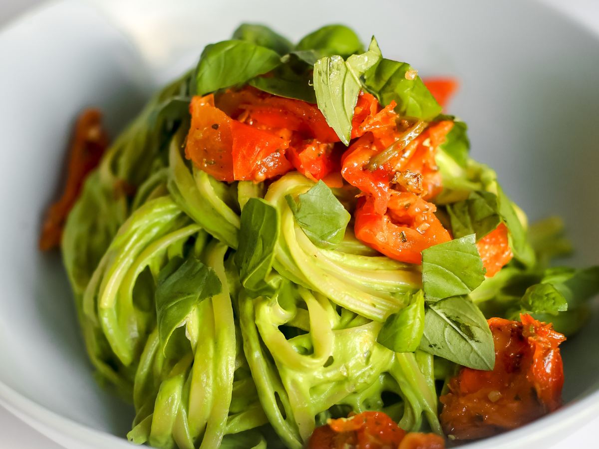 Bowl of green avocado pasta with tomatoes.