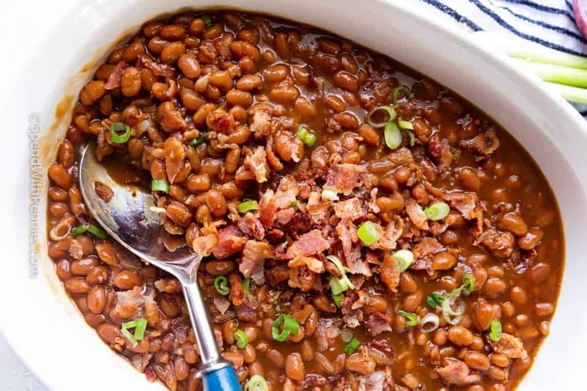 A bowl of baked beans with bacon and green onions.