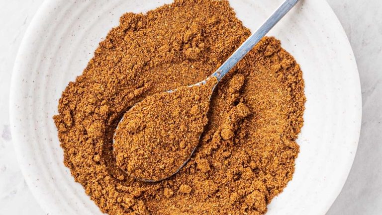 Cinnamon powder in a white bowl with a spoon.