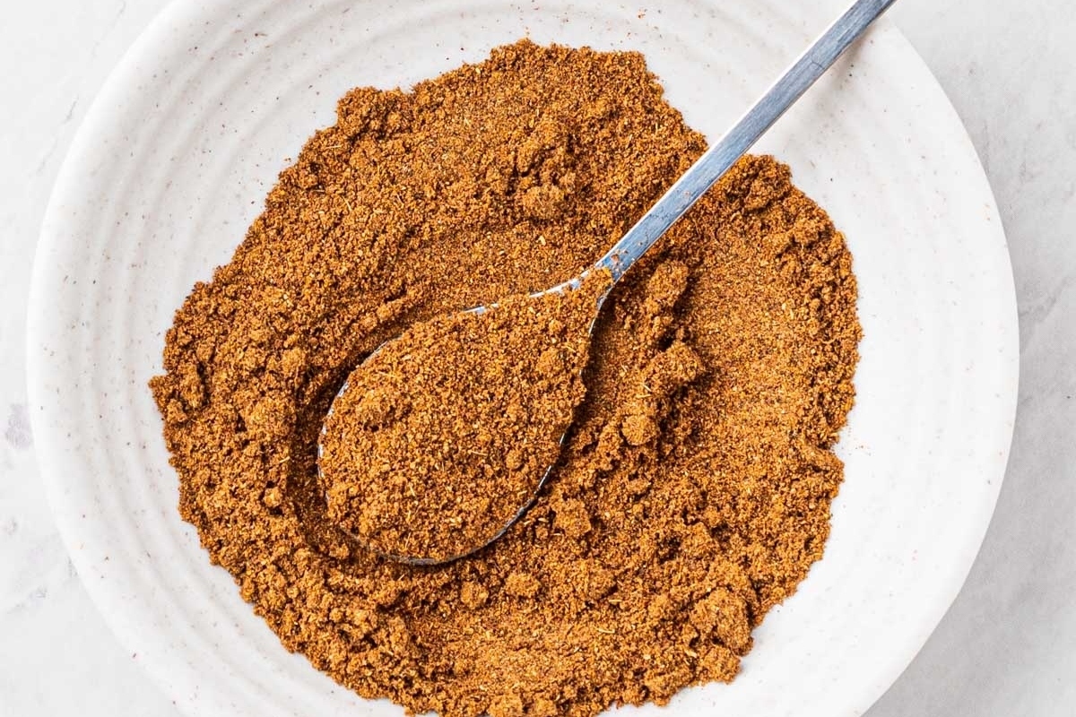 Cinnamon powder in a white bowl with a spoon.