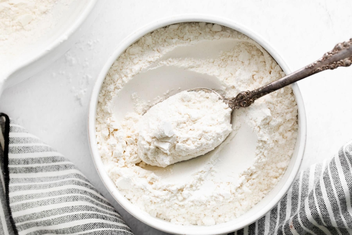A bowl of flour with a spoon next to it.