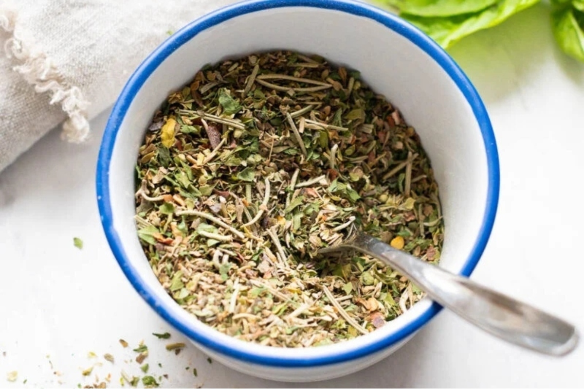 A bowl of herbs with a spoon next to it.