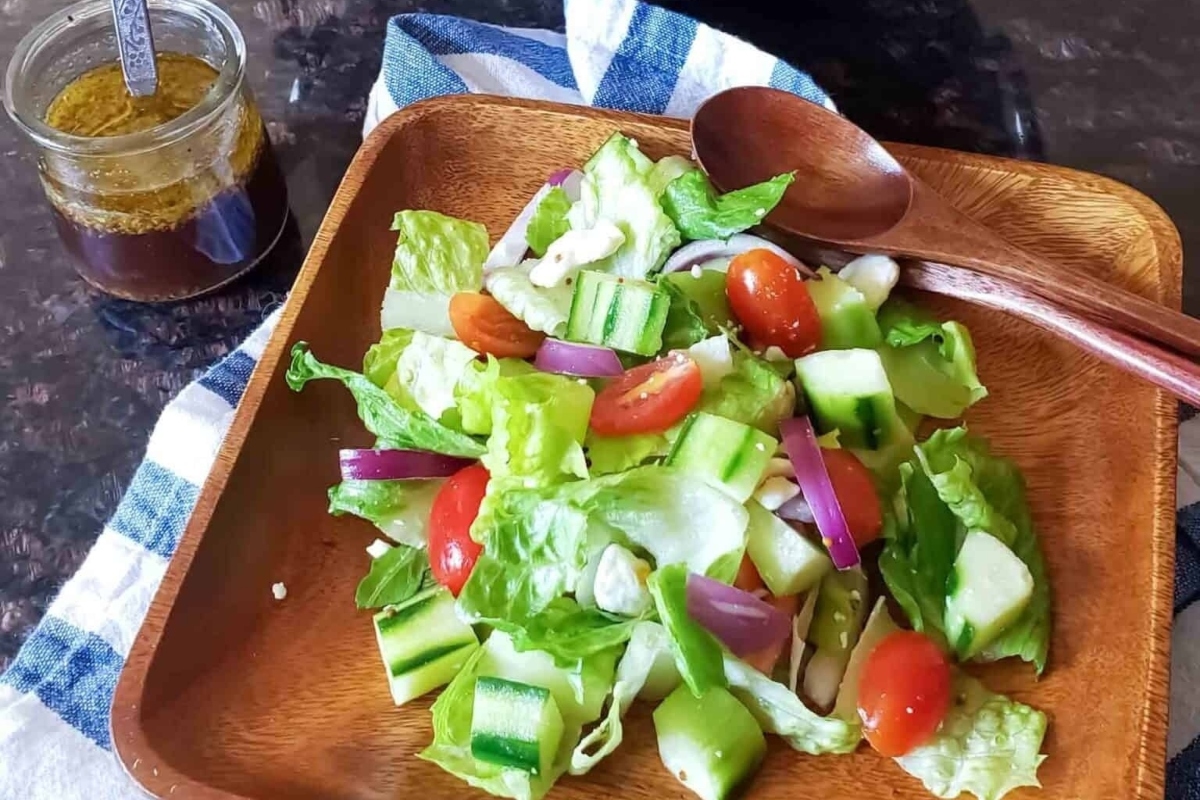 A salad on a wooden plate with a jar of dressing.