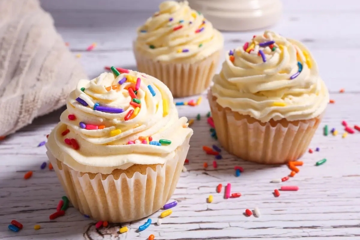 Three cupcakes with sprinkles on a wooden table.