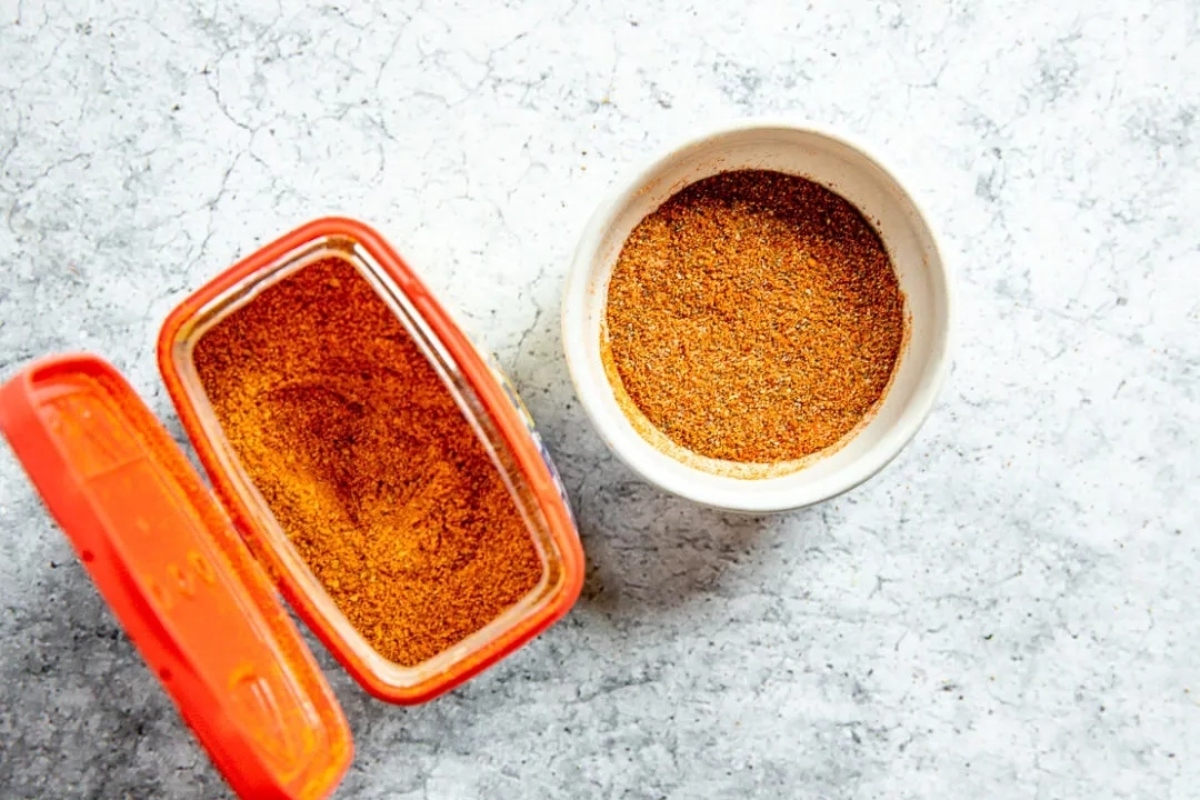 A bowl of spices next to an orange container.
