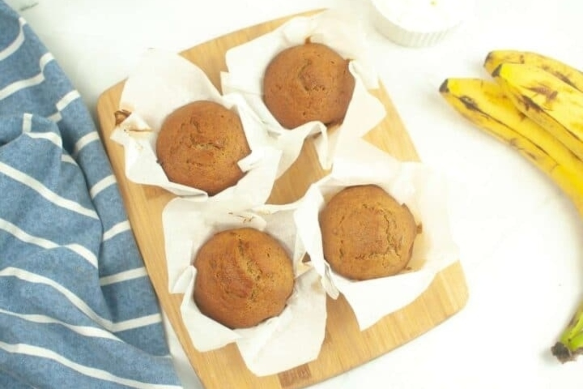Banana muffins on a cutting board next to bananas.
