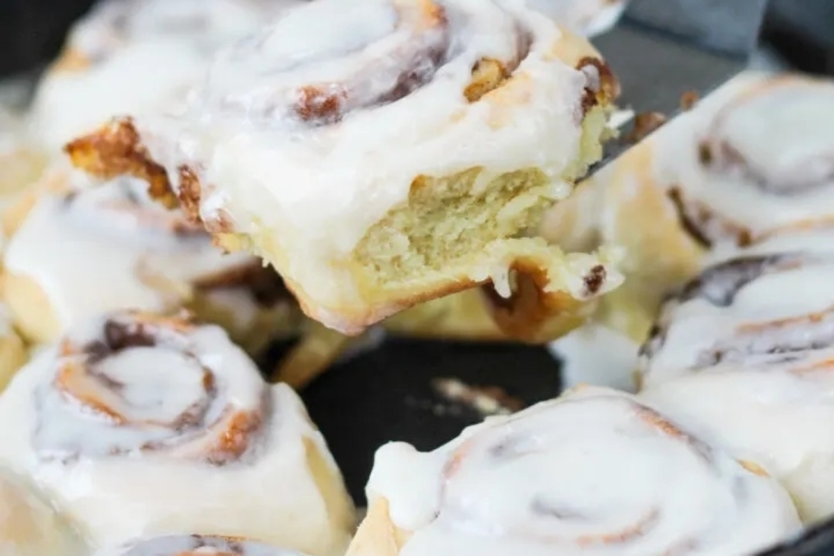 Cinnamon rolls being taken out of a skillet.