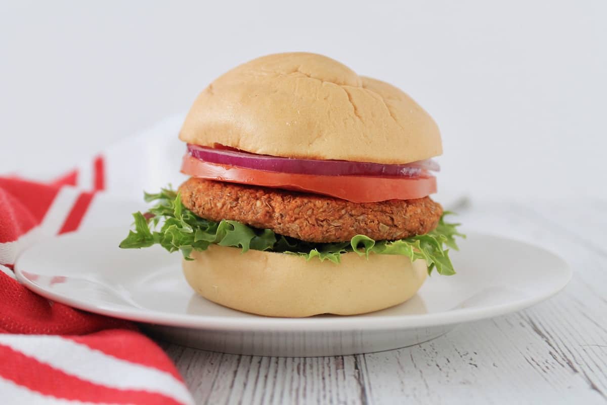 A lentil burger on a white plate with tomatoes and onions.