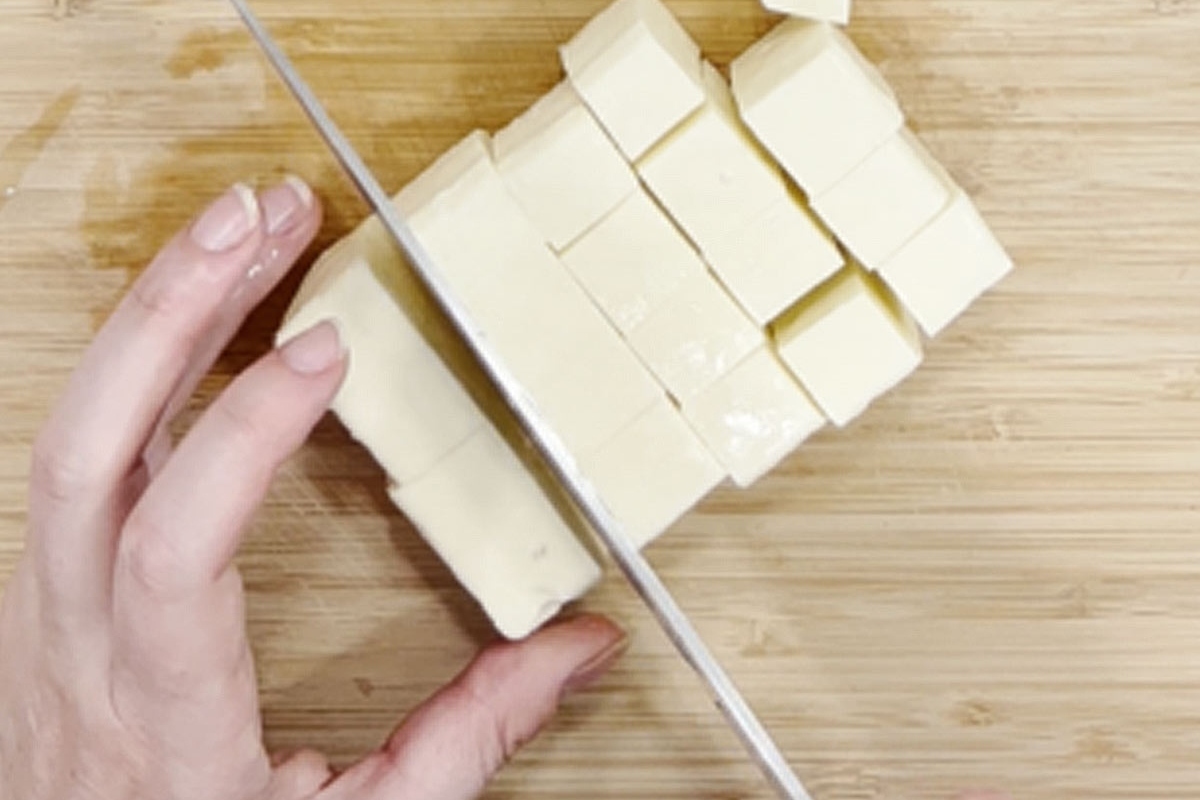 A person cutting paneer into cubes on a cutting board.