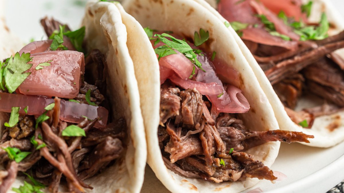 Three shredded beef tacos on a plate.