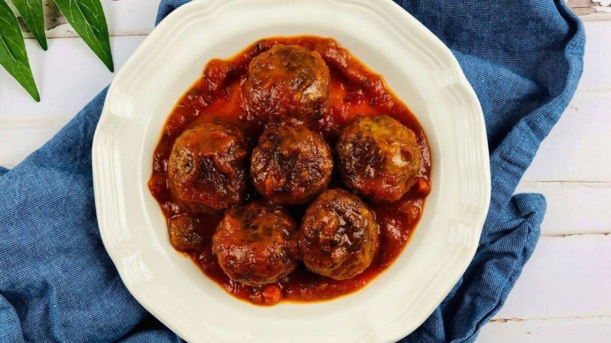 Meatballs covered in sauce on a white plate.