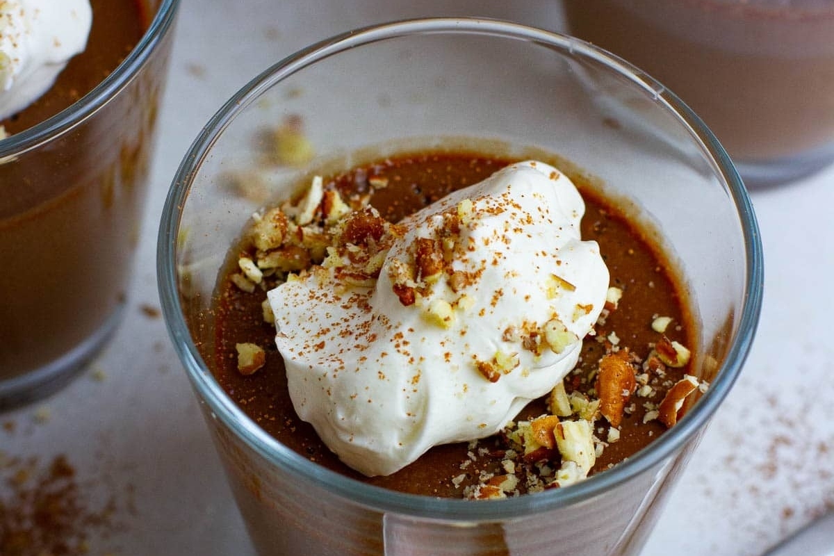 A glass of chocolate pudding with whipped cream and pistachios.
