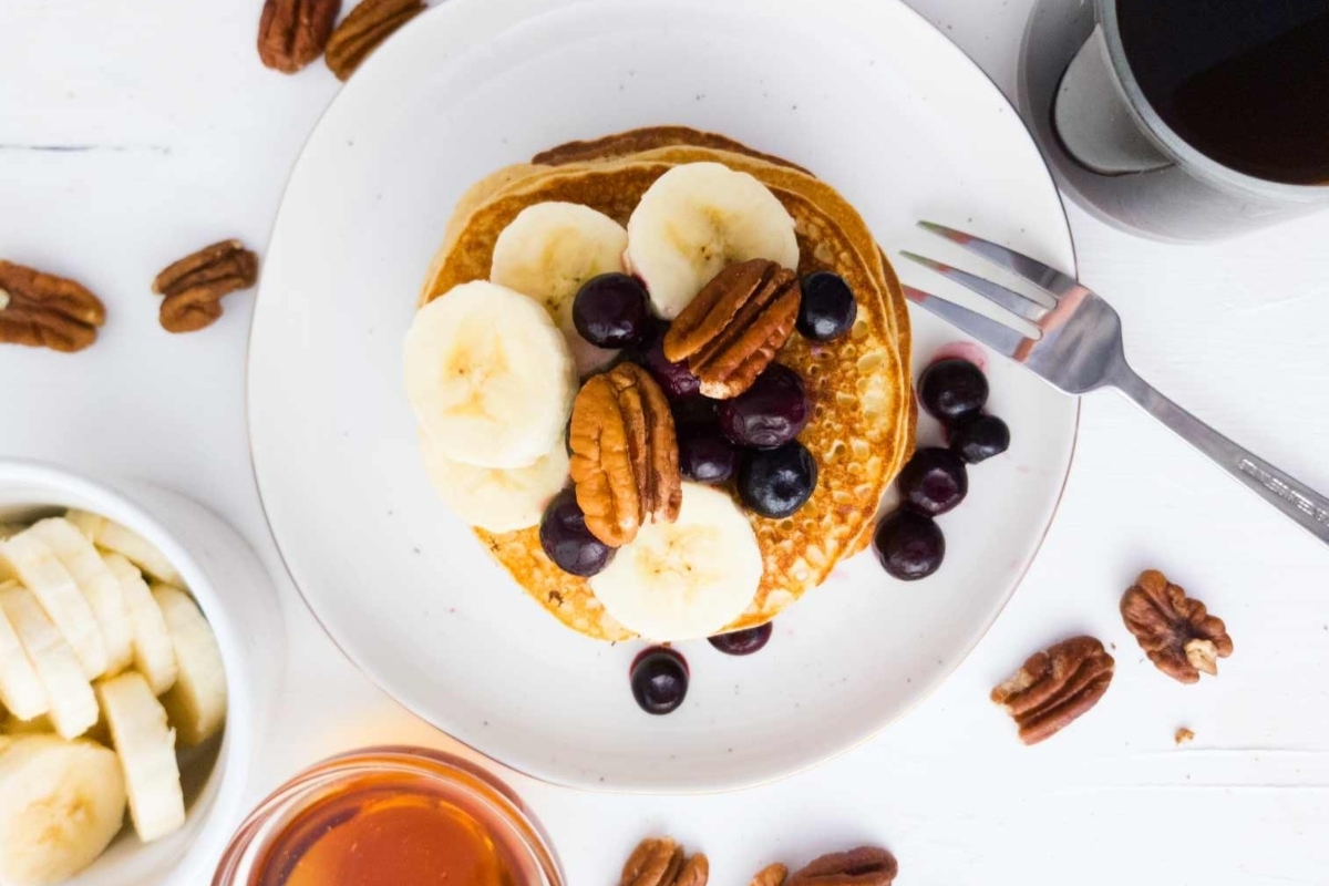 Pancakes with blueberries and pecans on a white plate.