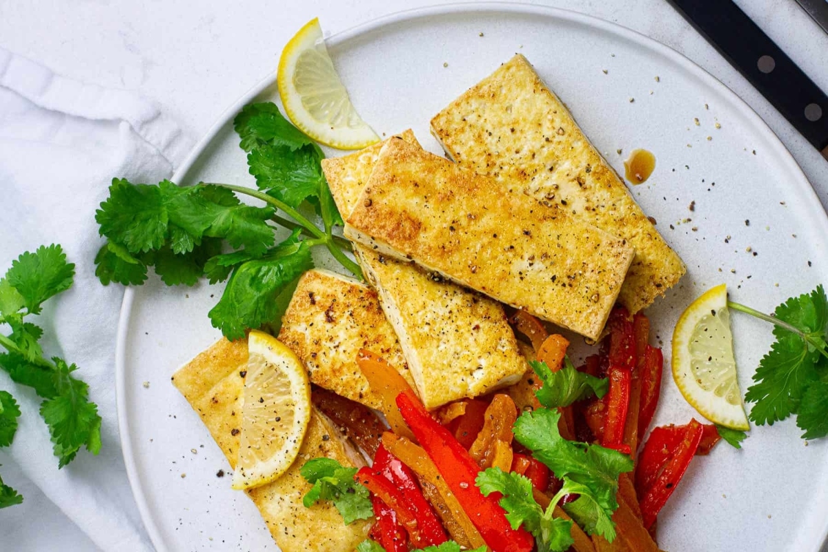 A plate with tofu, peppers and lemons on it.