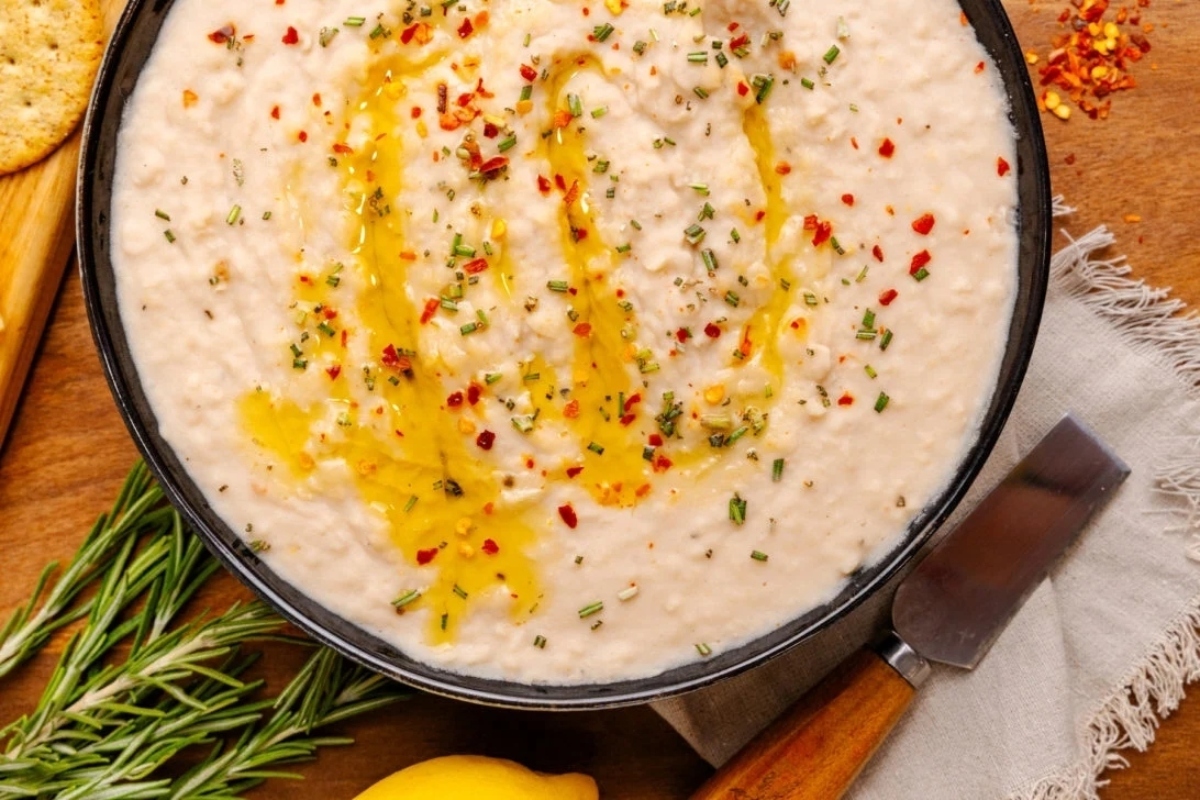 A bowl of white bean dip with a knife and fork.