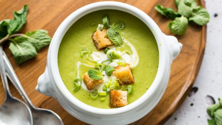 A bowl of green soup with croutons and mint.