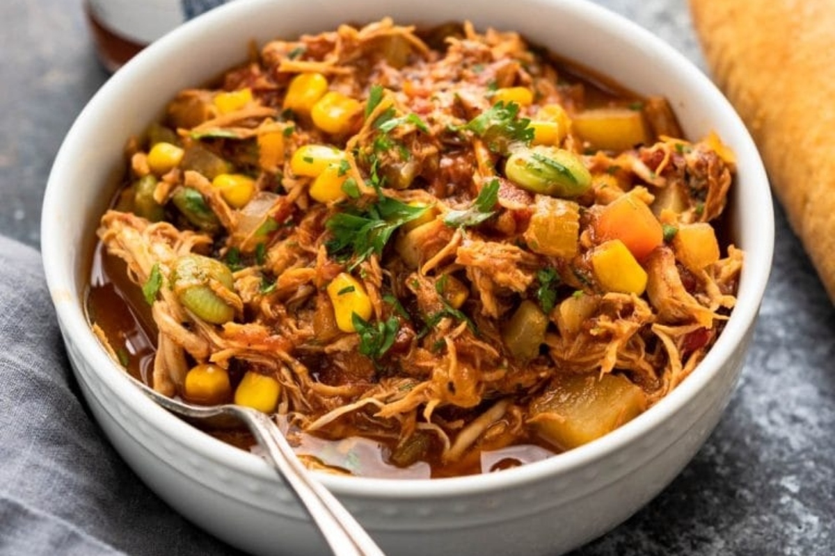 A bowl of chicken stew with vegetables and a spoon on the side.