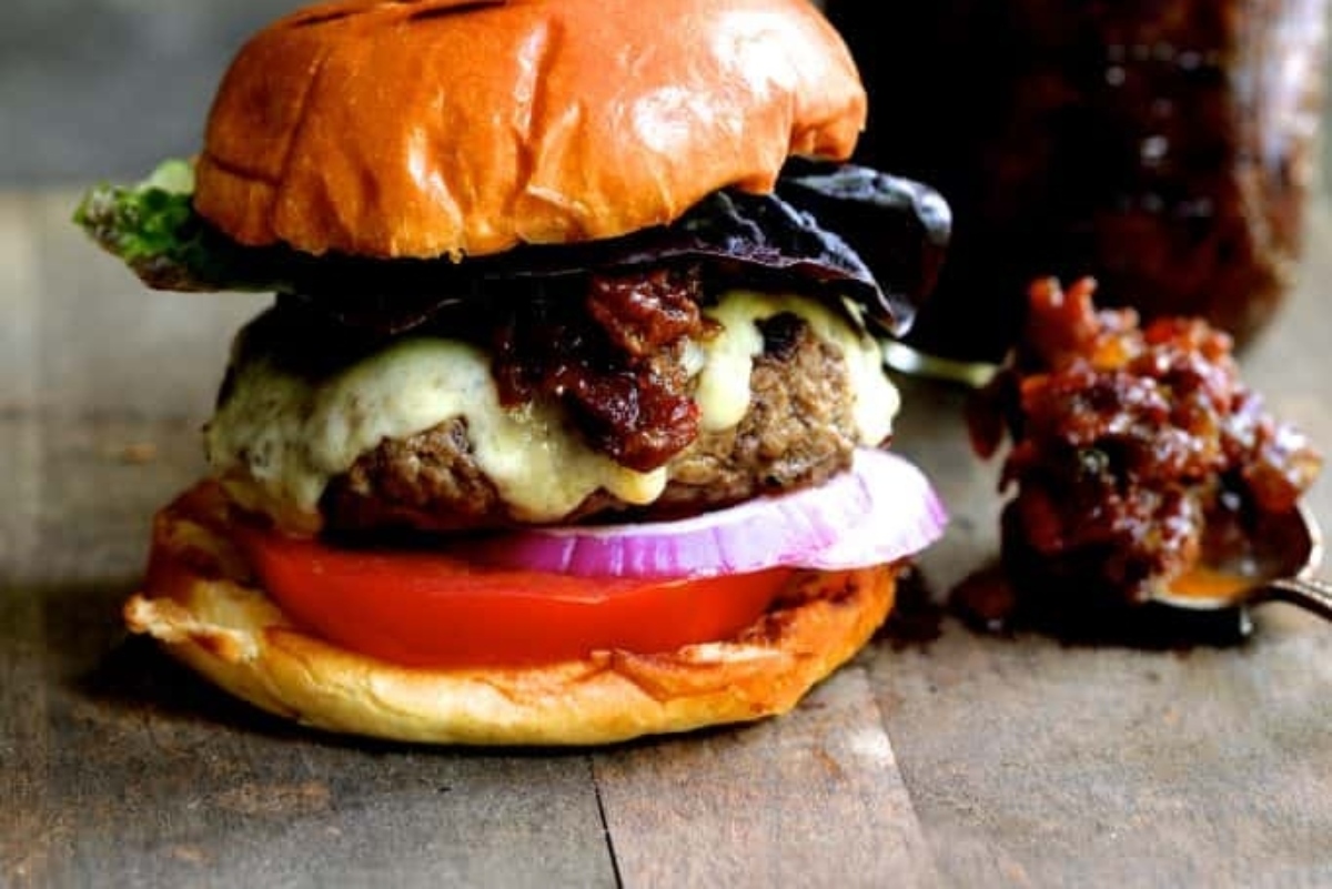 A burger with tomatoes, onions, and ketchup on a wooden table.