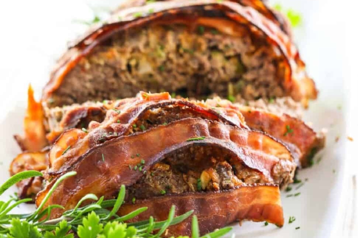 Bacon wrapped meatloaf on a white plate.