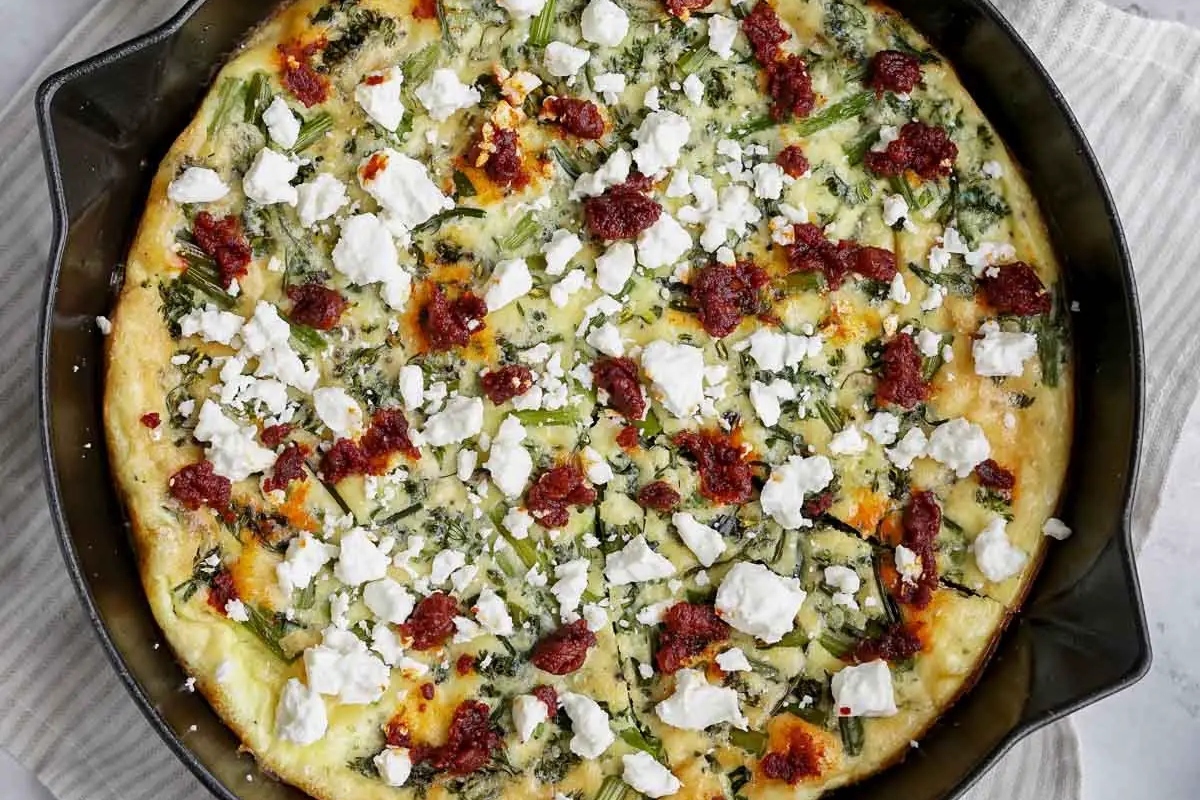 A freshly baked frittata with spinach, sun-dried tomatoes, and crumbled feta cheese in a cast iron skillet.