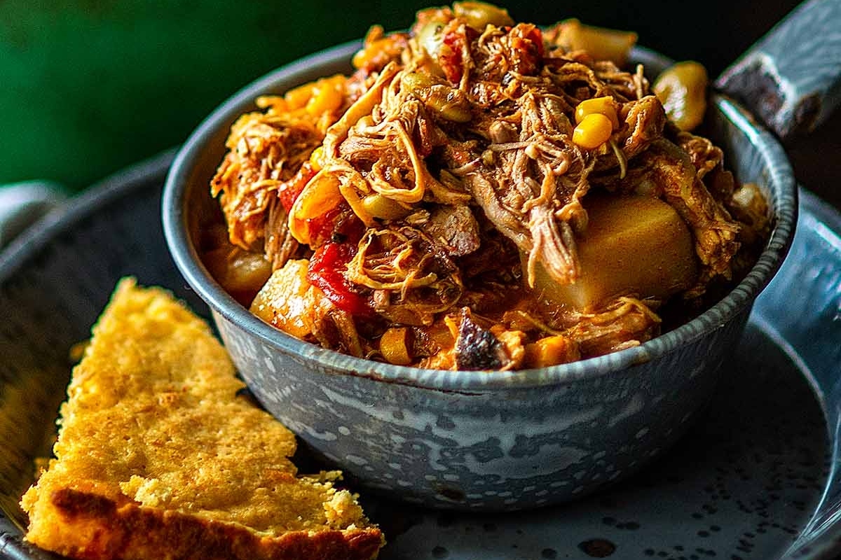 A bowl of food next to a piece of cornbread.