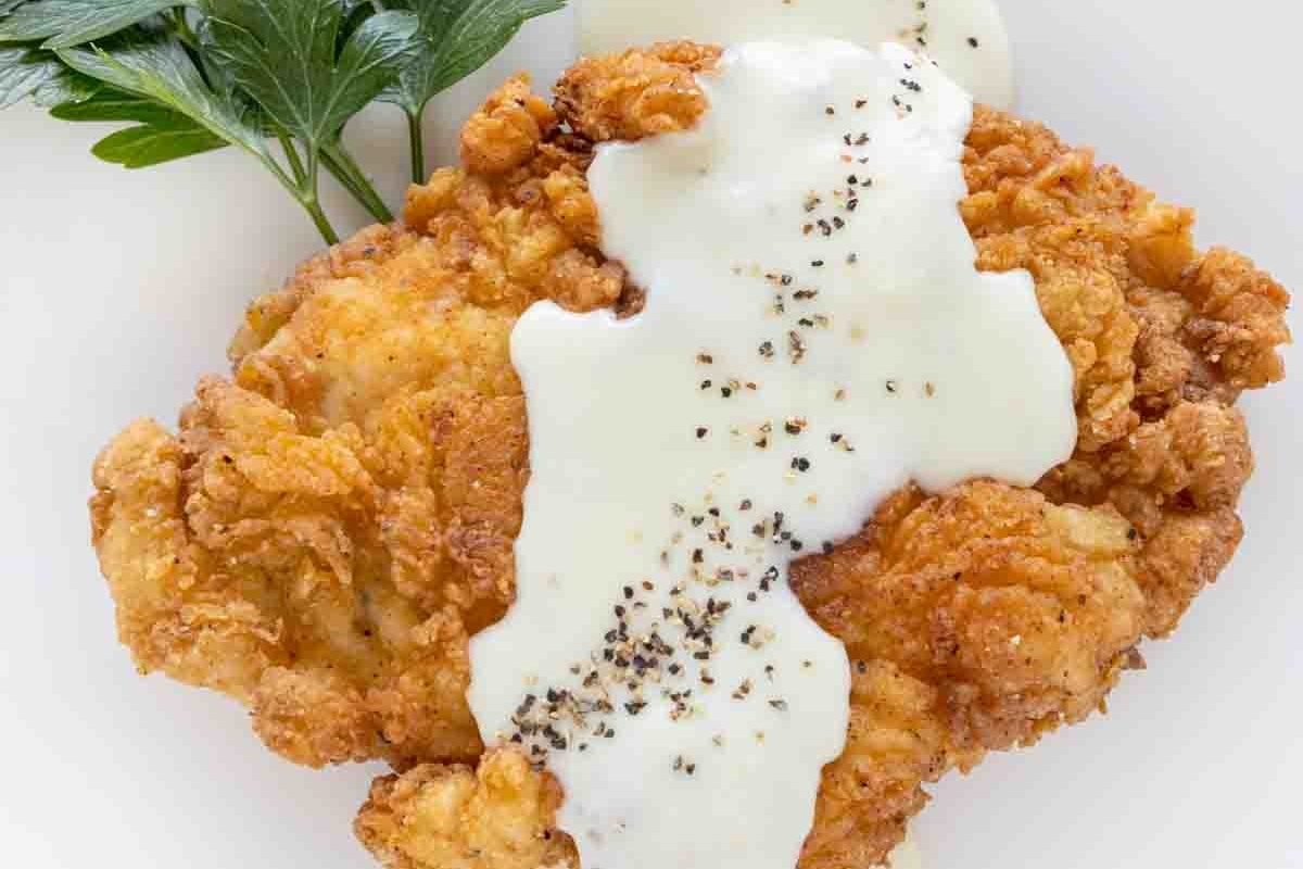 Fried chicken cutlet with creamy white gravy and a garnish of parsley on a white plate.