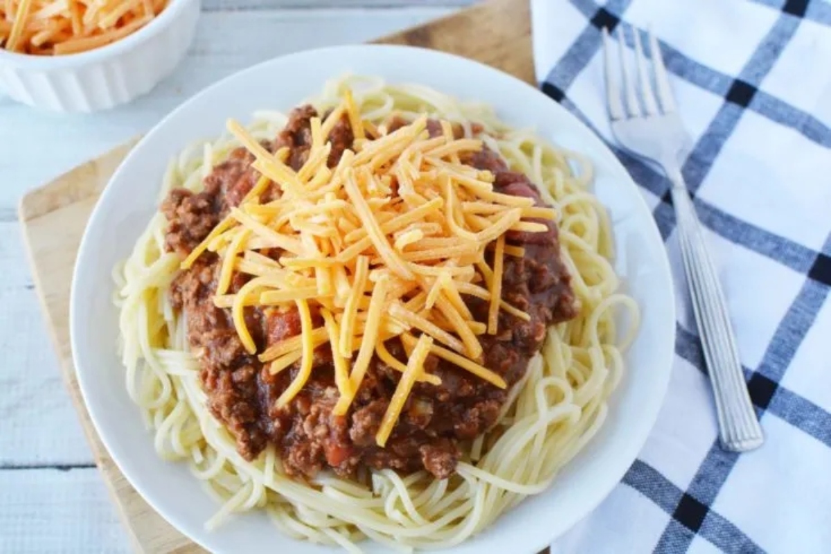 A plate of spaghetti topped with meat sauce and shredded cheddar cheese.