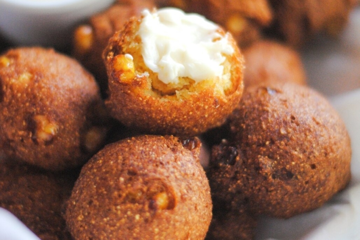 A close-up of golden-brown hushpuppies served with a dollop of creamy sauce.