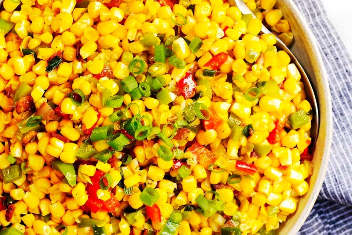 A bowl of sautéed corn with diced red peppers and sliced green onions.