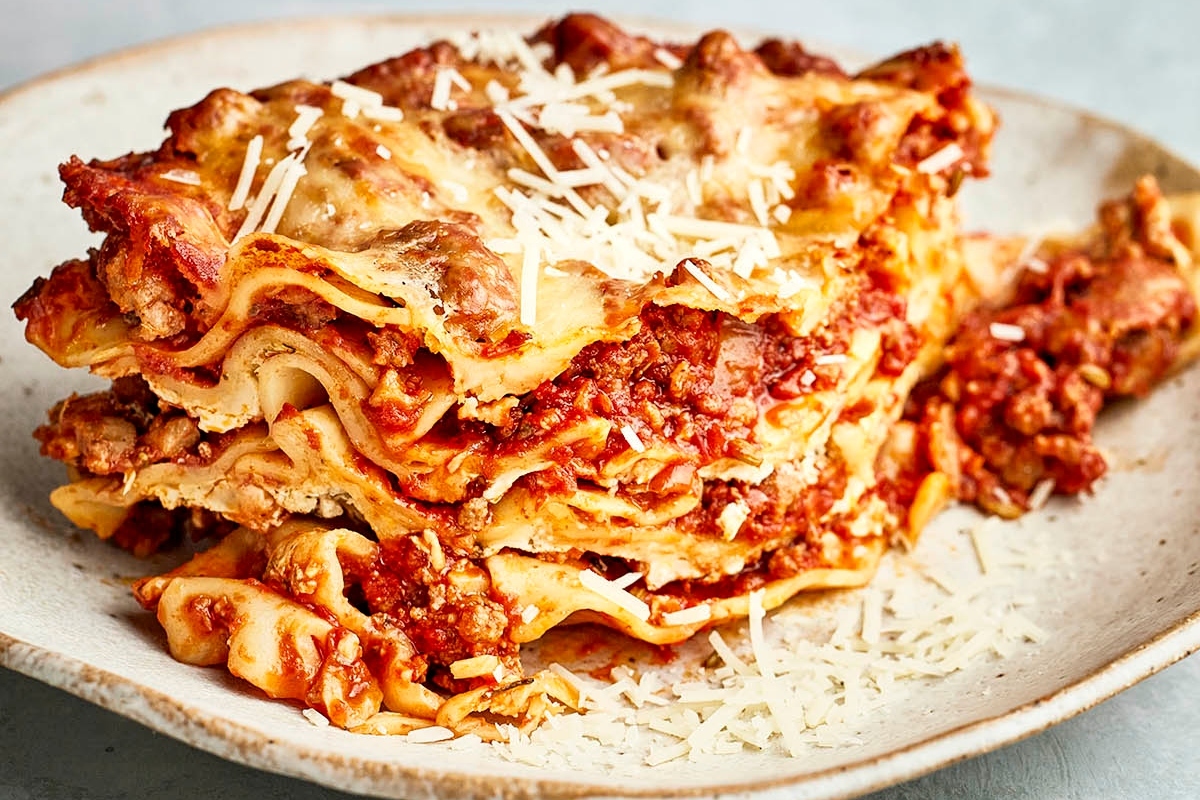 A slice of lasagna with layers of pasta, meat sauce, and melted cheese, served on a plate with grated cheese on top.