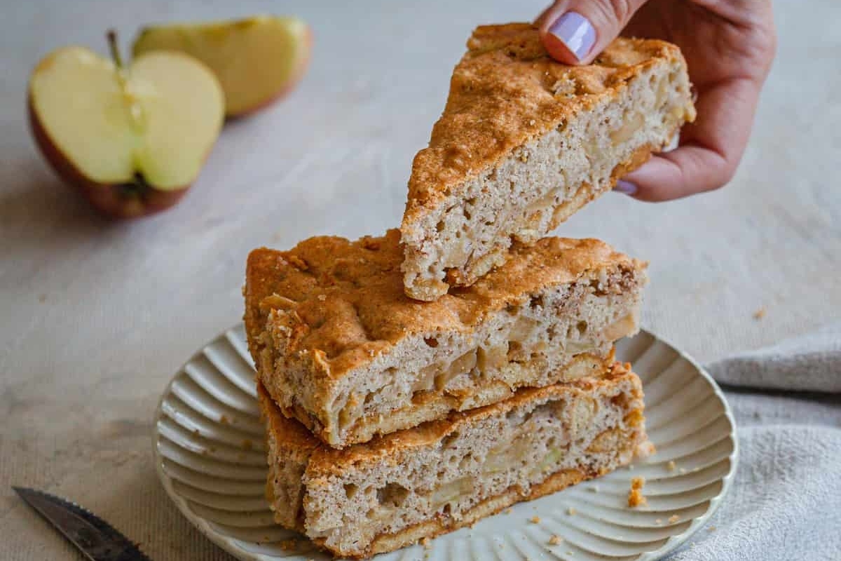 A person is holding a slice of apple scones on a plate.