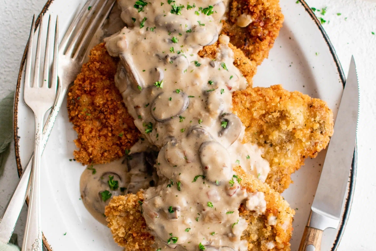 A plate of crispy fried pork with creamy mushroom gravy and a sprinkle of herbs.