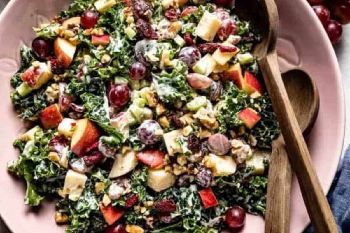 Kale salad with apples and grapes in a pink bowl.