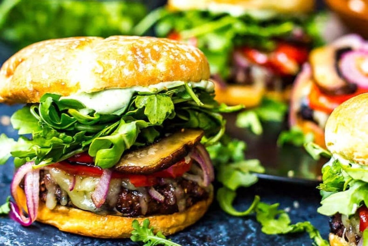 Burgers with vegetables and herbs on a black plate.