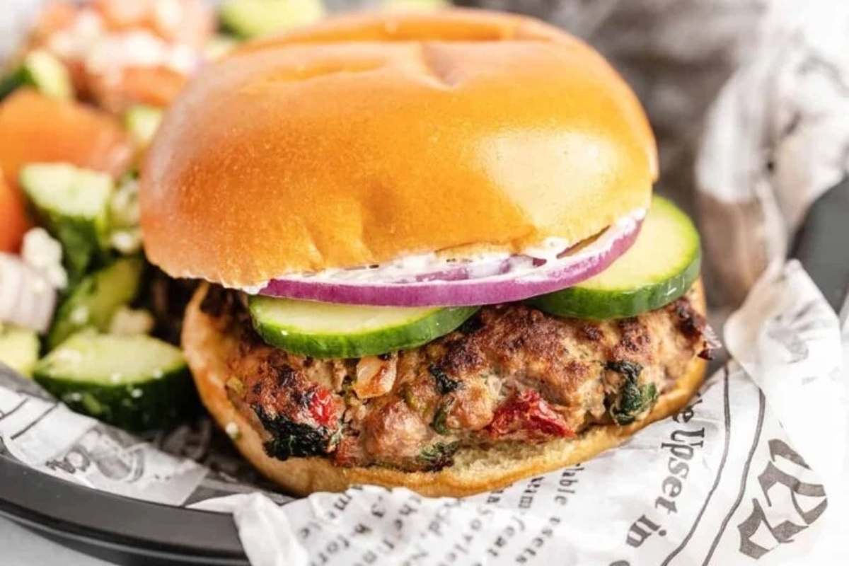 A burger with lettuce, tomatoes and cucumbers.