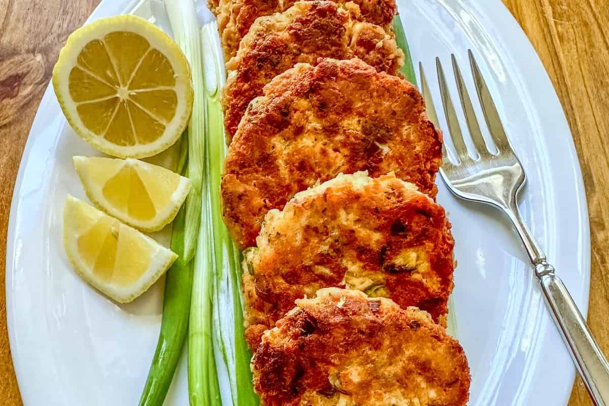 A plate of crispy fried salmon cakes served with lemon wedges and green onions.