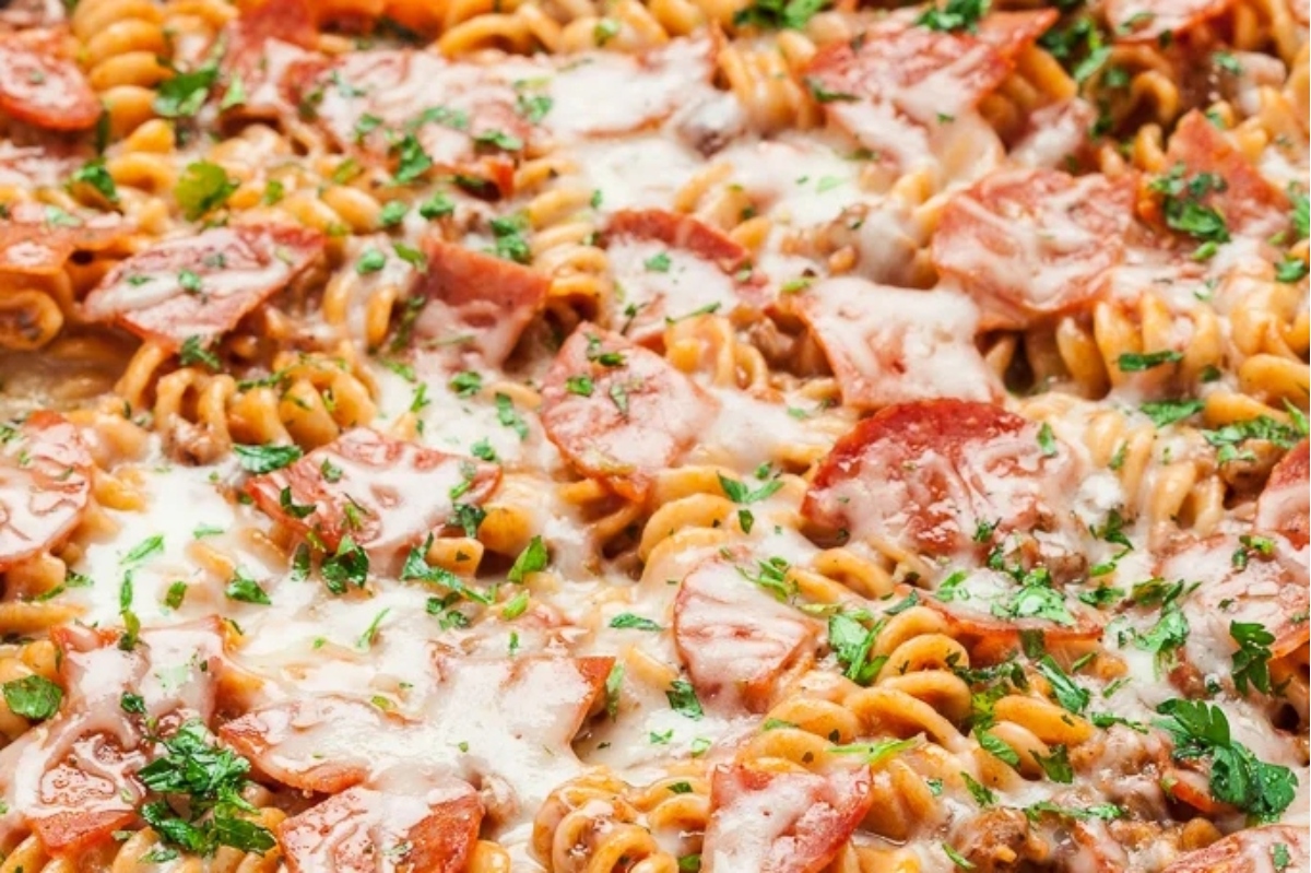 A close-up of a cheesy pasta dish with tomato sauce, pepperoni, and garnished with parsley.