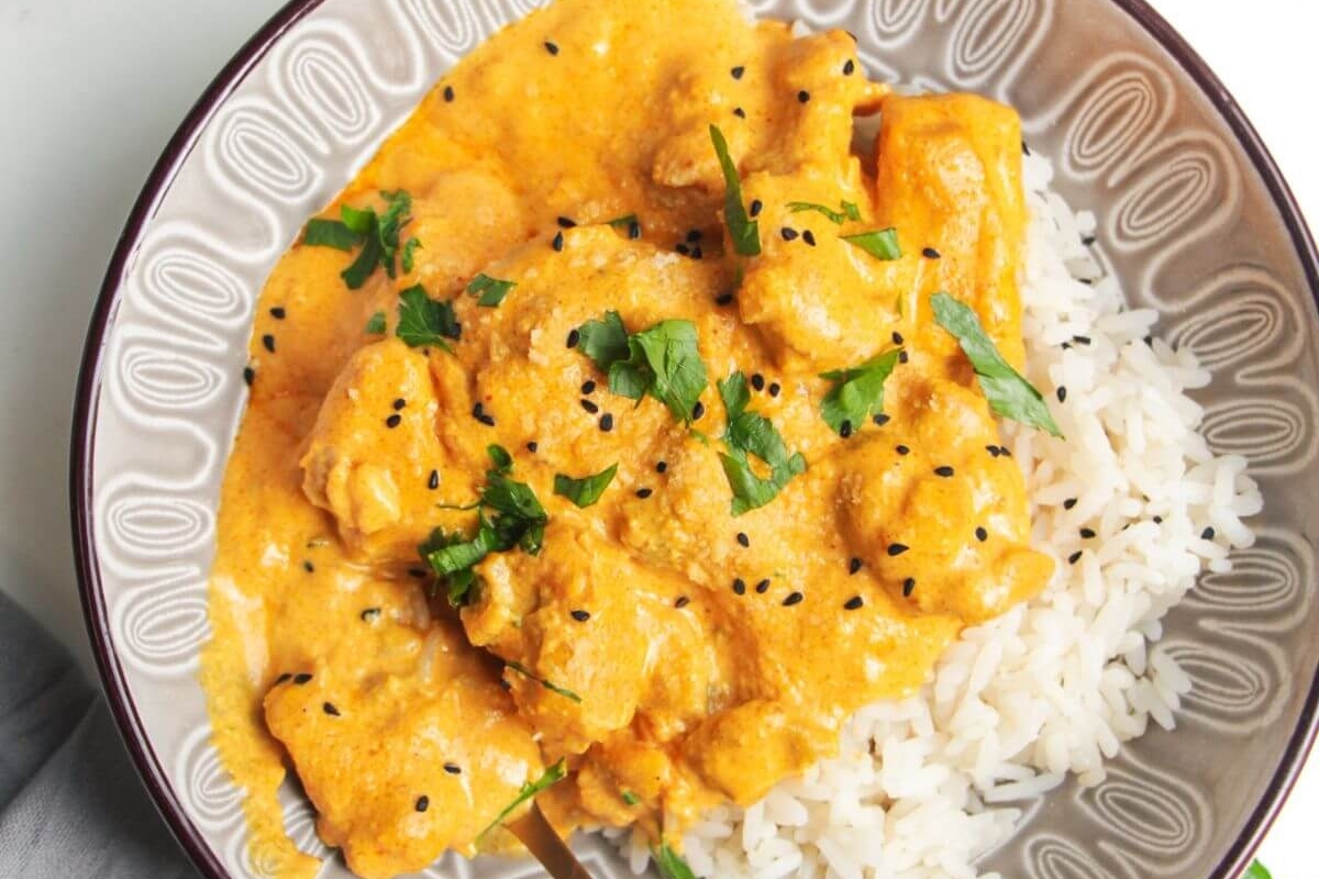 A bowl of chicken curry served over white rice, garnished with chopped cilantro.