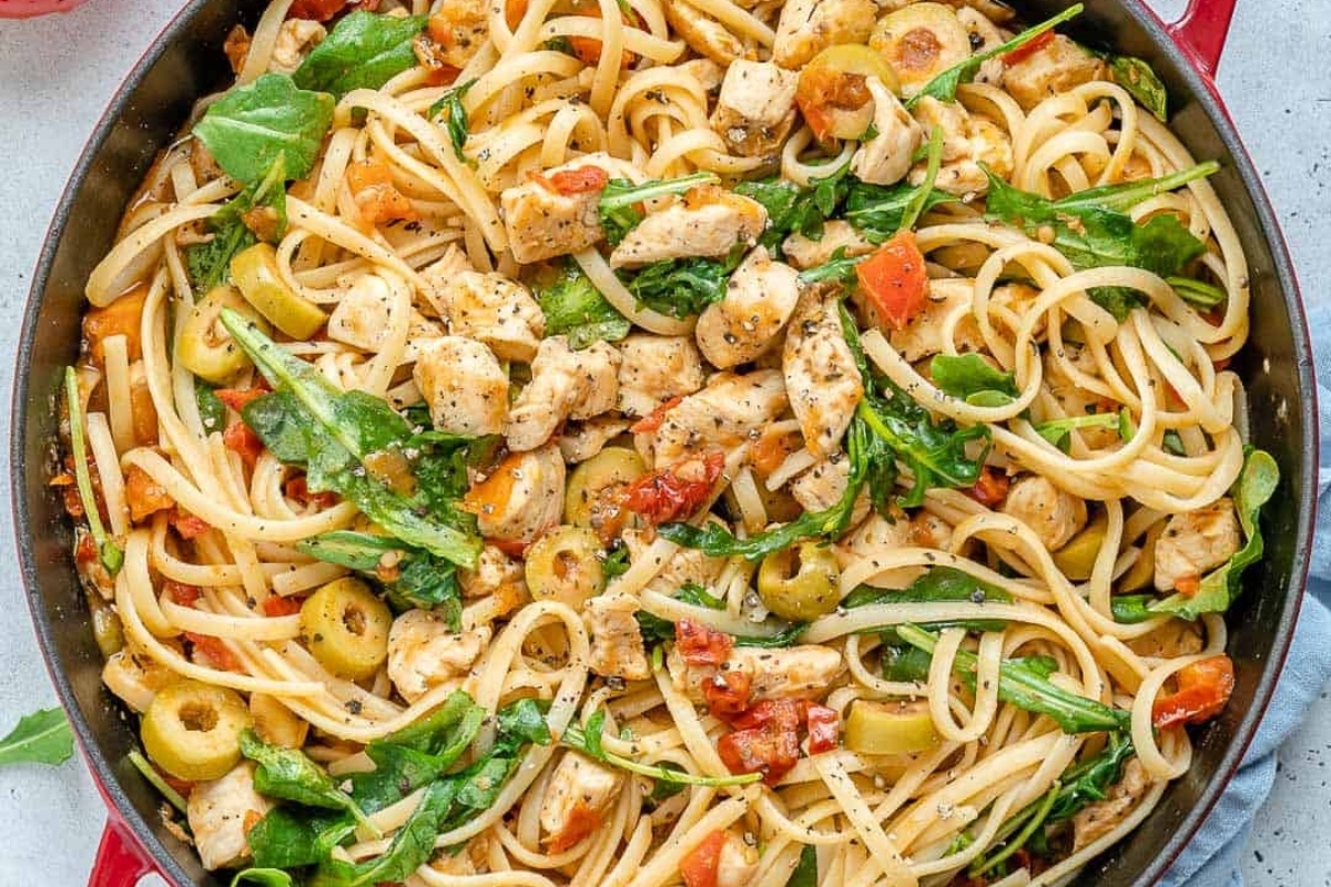 Fettuccine pasta with chicken, olives, tomatoes, and spinach in a skillet.