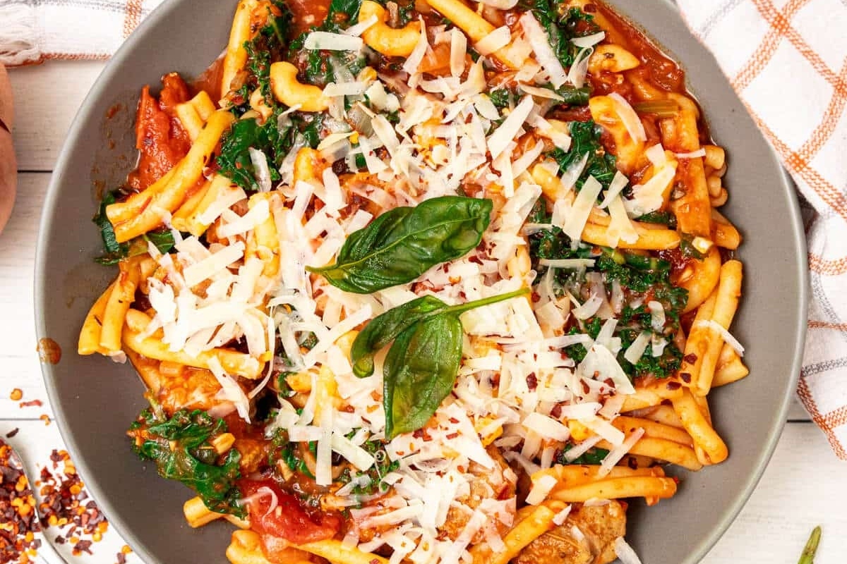 A bowl of pasta with tomato sauce, kale, and grated cheese garnished with basil leaves.