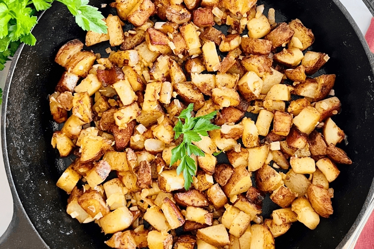Diced potatoes sautéed to a golden brown in a skillet, garnished with parsley.