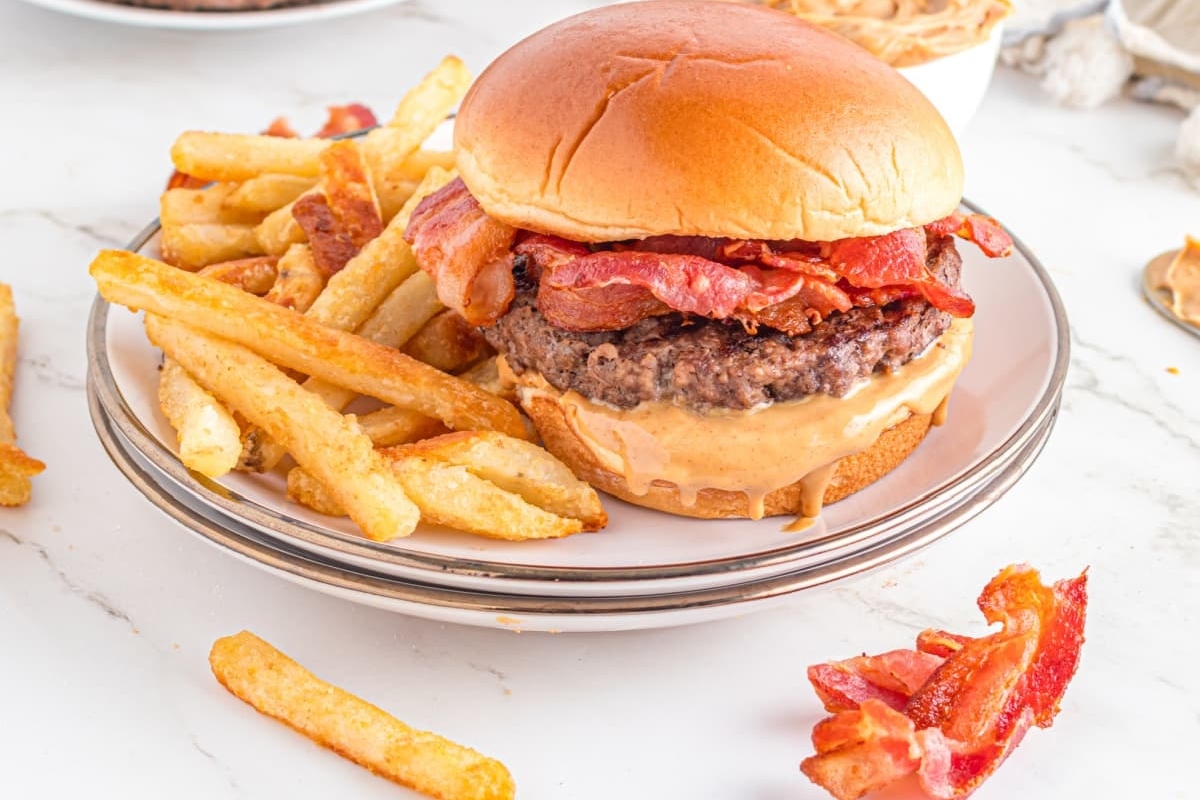 A burger with bacon and fries on a plate.