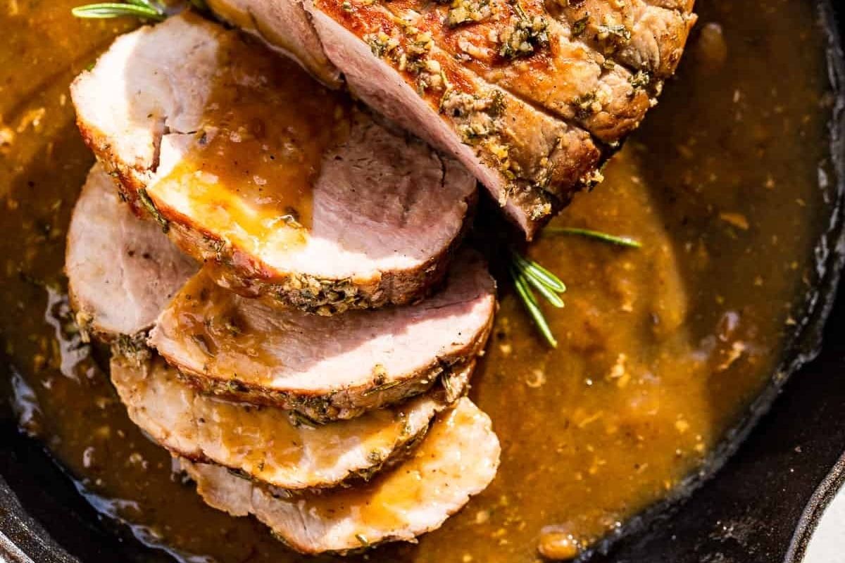 Sliced roasted pork loin with herbs in a pan.