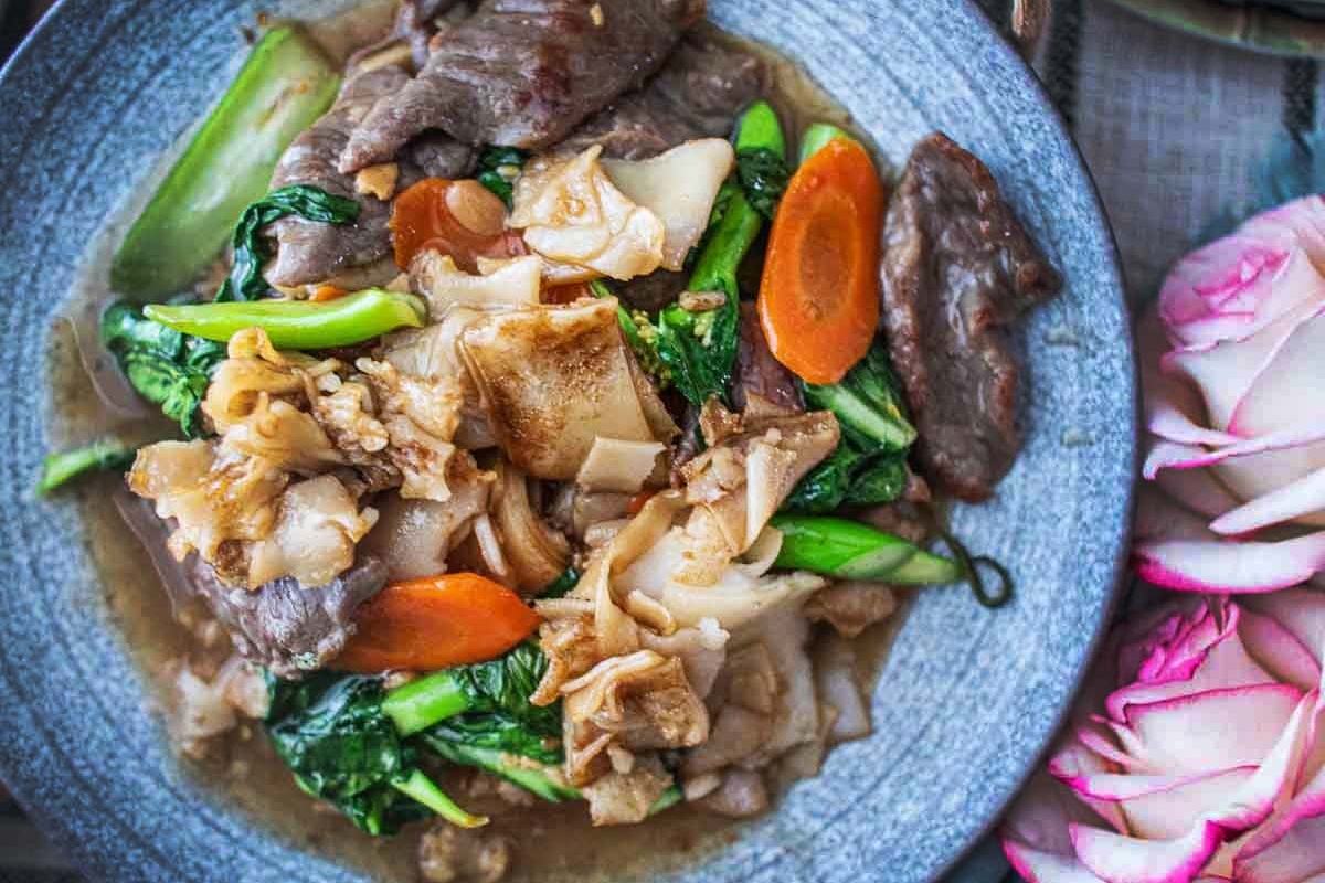 A bowl of stir-fried vegetables and meat with a side of pickled radishes.