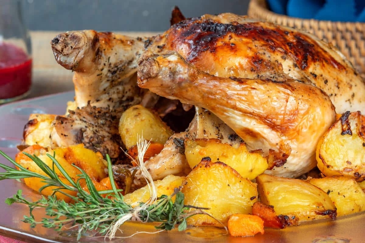 Roasted chicken with herbs and golden potatoes on a plate.