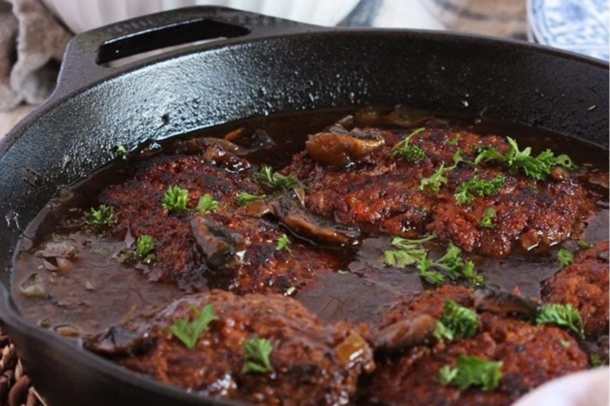 Cooked salisbury steak in a sauce garnished with herbs in a cast iron skillet.