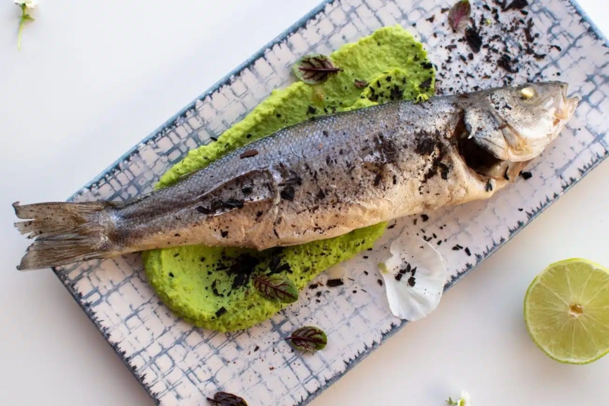 A fish on a plate with lime and green sauce.