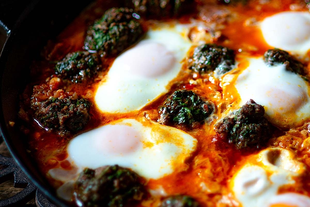 A skillet with simmering tomato sauce, meatballs, and poached eggs.